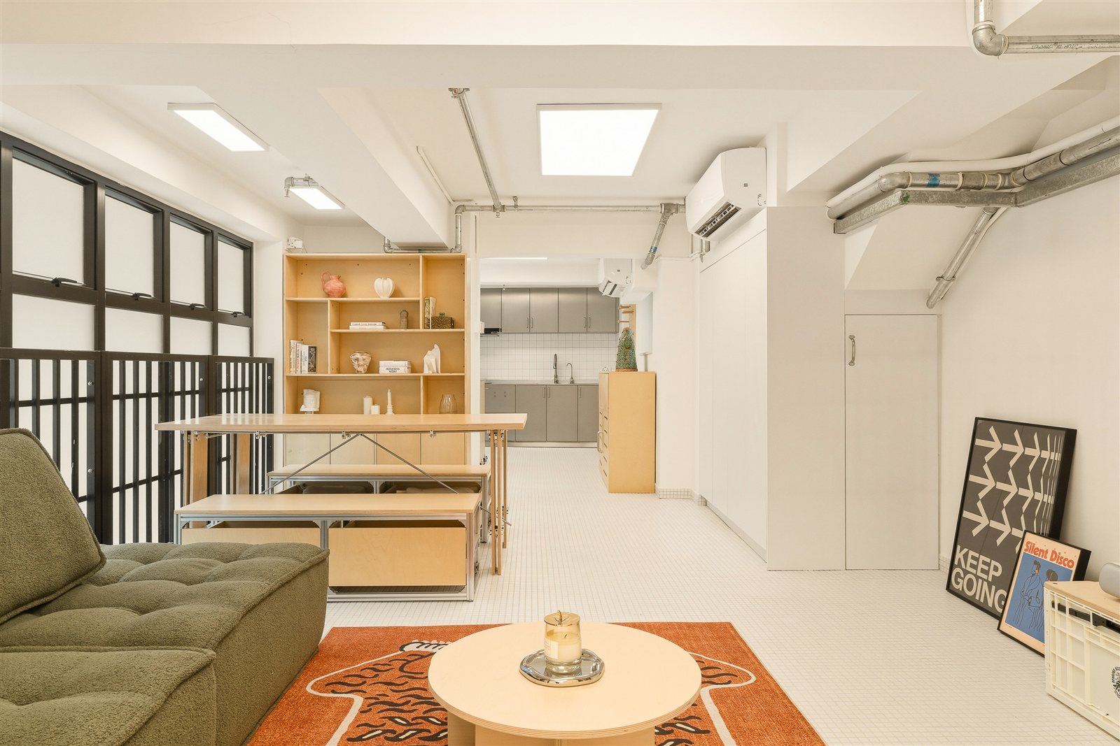 Open-plan living room with plywood shelving, green sofa, and steel-framed windows