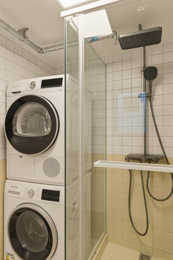 Compact bathroom with white tiles, glass shower, and stacked washer-dryer
