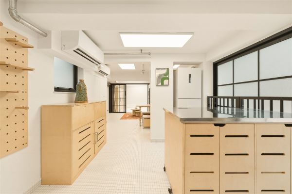 Kitchen corridor with plywood cabinetry, pegboard wall, and living area beyond