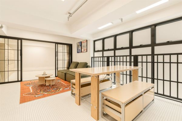 Living and dining space with green sofa, plywood table, and black steel-framed windows