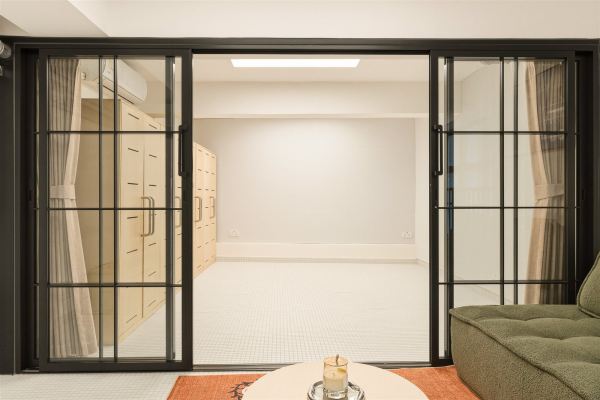 Black steel-framed sliding doors opening to bedroom with plywood wardrobe